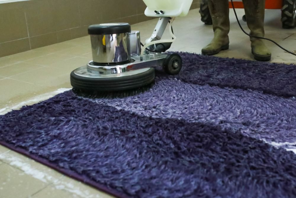 A person cleans a purple rug with a machine, representing a rug cleaning service in Columbia, SC.