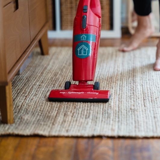 A woman uses a red cordless vacuum on a rug, representing a carpet cleaning service based in Columbia, SC.