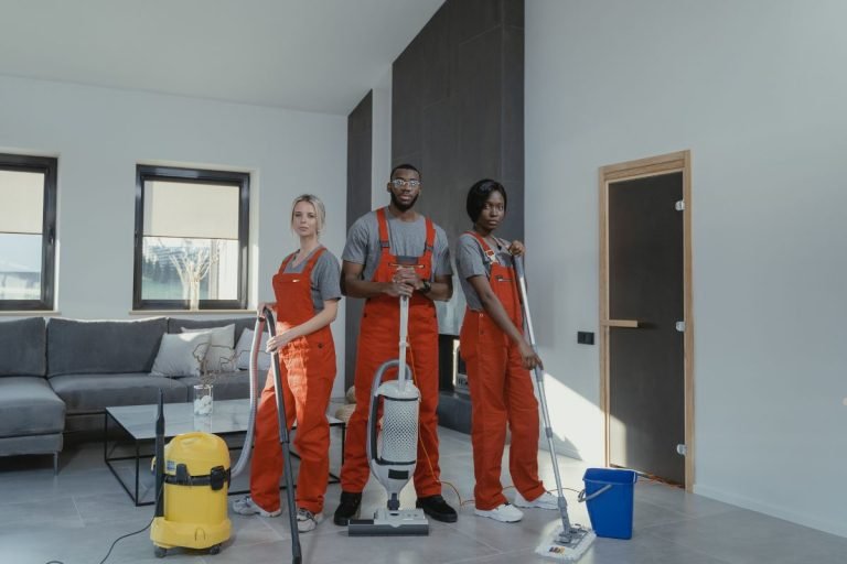 Three individuals in overalls cleaning a room, focusing on carpet cleaning with equipment and tools.