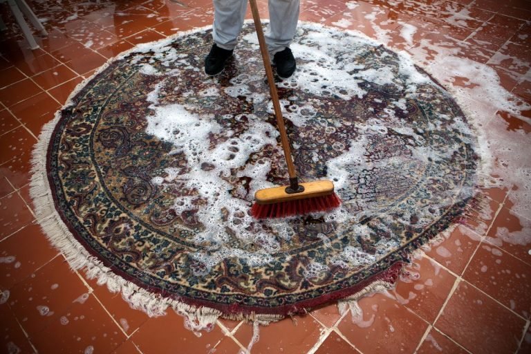 A person using a broom to clean a rug, representing a professional carpet cleaning service in action.
