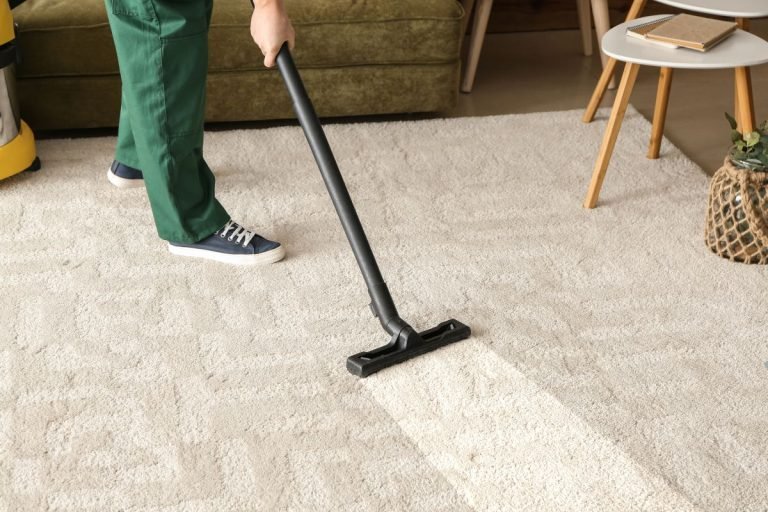 A person using a vacuum cleaner to clean a carpet in a well-lit room, focusing on removing dirt and debris.
