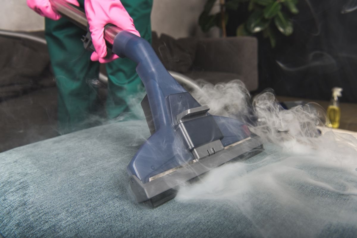 A person wearing green gloves vacuums a couch, removing dust and debris for a clean living space.